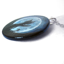 Load image into Gallery viewer, A lightweight wooden pendant necklace is hand painted with art of the silhouette of a black cat, with a front paw reaching up, sitting in front of a large full moon.
