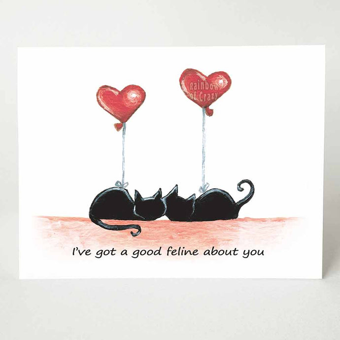 a greeting card with two black cats curled up next to each other, each having a heart shaped balloon tied to them. The card reads, 