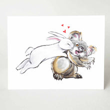 Load image into Gallery viewer, a greeting card of a white rabbit leaping onto a surprised koala and giving it kisses
