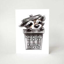 Load image into Gallery viewer, a birthday greeting card with art of a baby raccoon peeking out from a garbage can. the card reads, &quot;stealing hearts. eating trash&quot; on the front and
