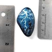 Load image into Gallery viewer, a beach rock with cat art: a black cat on a cliff, looking out into the night sky filled with lightning. the stone is next to two rulers to show its size: 1 9/16&quot; x 1&quot; or 4 cm x 2.5 cm
