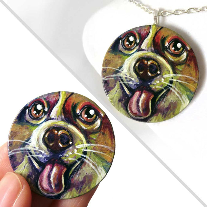 A circle wood pendant featuring a portrait of a corgi in all the colours of the rainbow. Available as either a keepsake or a necklace