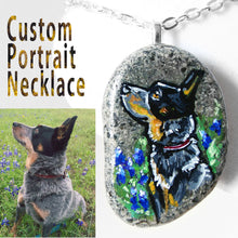 Load image into Gallery viewer, A custom pet portrait necklace, painted on a beach stone, of an Australian Cattle Dog, sitting in a field of flowers.
