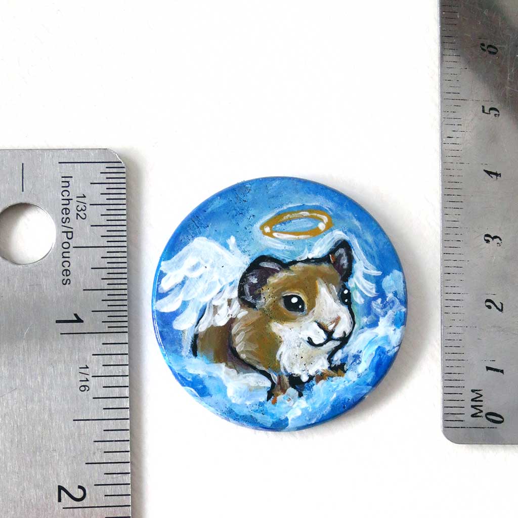 a miniature wood painting of a brown and white guinea pig angel, next to two rulers to show its size: 1 1/2 inches or 3.8 cm across