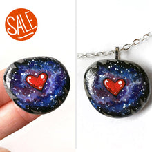 Load image into Gallery viewer, a beach stone has been hand painted with a heart surrounded by outer space and stars, and hand crafted as either a keepsake stone or pendant necklace
