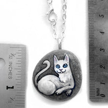 Load image into Gallery viewer, The white cat portrait necklace, hand painted on a small beach rock, next to try rulers to show its size: 1 1/4&quot; x 1 1/8&quot; or 3.1 cm x 2.8 cm 
