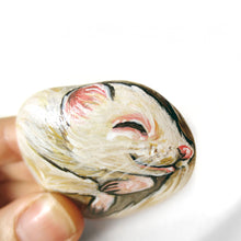 Load image into Gallery viewer, A hand holding a small rock art of an albino ferret sleeping.

