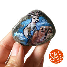 Load image into Gallery viewer, Rock art featuring a painting of a ram on a mountain, in front of a cloudy blue sky. The symbol for Aries is painted on the bottom.
