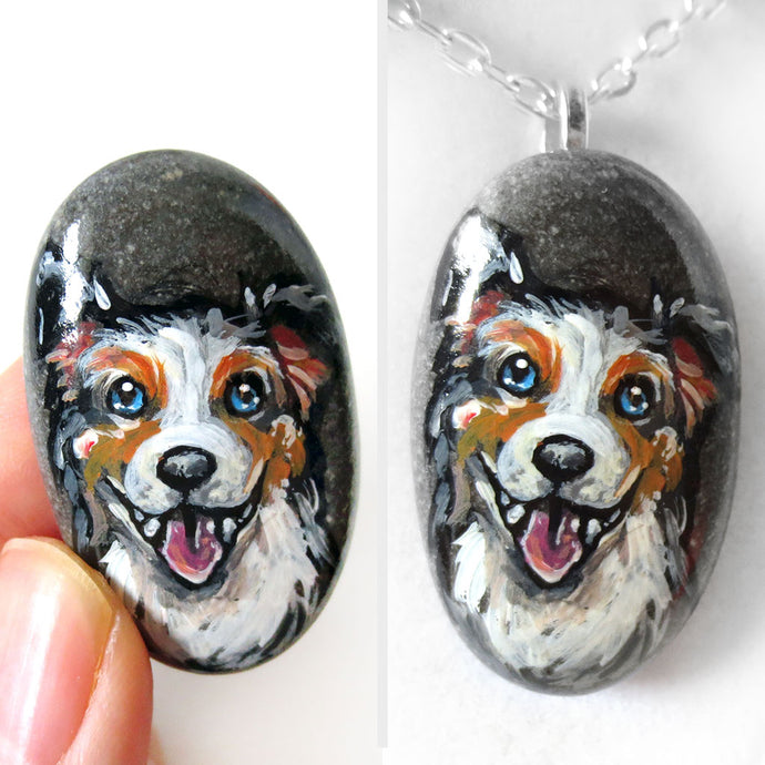 a small beach rock, hand painted with art of a smiling Australian Shepherd dog, available as a stone keepsake or pendant necklace. 