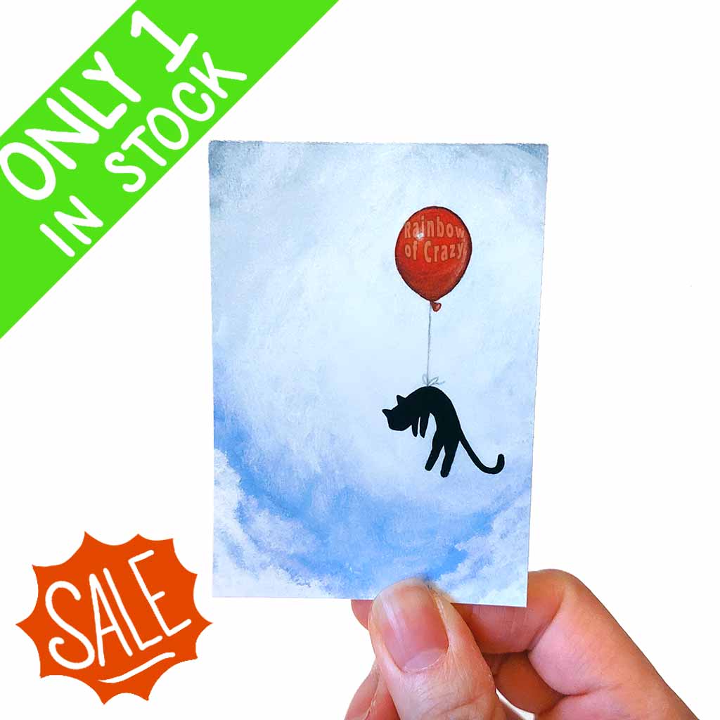 an aceo art print featuring a back cat floating through the sky, hanging onto a red balloon 