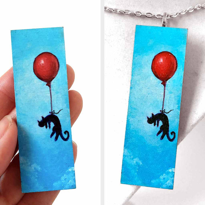 a wood rectangle hand painted with art of a black cat, with a red balloon, floating through a blue sky. available as a keepsake or pendant necklace