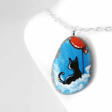 Load image into Gallery viewer, a small beach stone, hand painted with a little black cat, with a red balloon, sitting on clouds against a blue sky. available as a keepsake or pendant necklace
