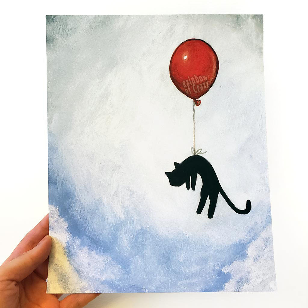 an art print with an illustration of a silhouette of a black cat, attached by the waiste to a big red balloon, as it floats through a blue cloudy sky