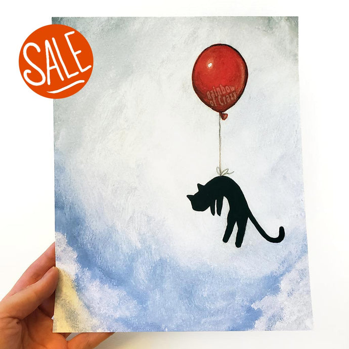 an art print with an illustration of a silhouette of a black cat, attached by the waiste to a big red balloon, as it floats through a blue cloudy sky