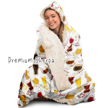 Load image into Gallery viewer, a woman wears the Beer Lovers Hooded Blanket, lined with premium sherpa: a white hooded blanket printed with a variety of different beer styles in different glasses
