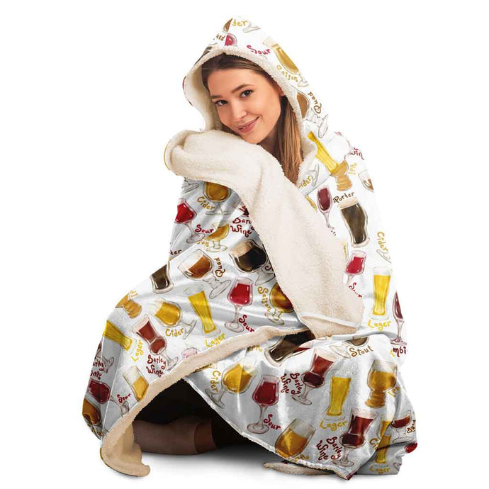 a woman wears the Beer Lovers Hooded Blanket, lined with microfiber fleece: a white hooded blanket printed with a variety of different beer styles in different glasses