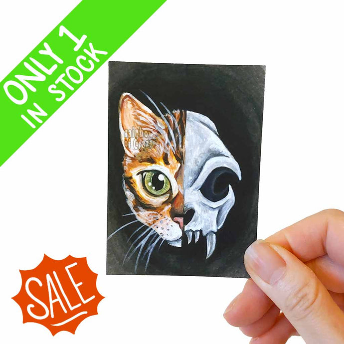 This ACEO art print features a split image: a bengal cat's face on the left side, and a stylized scary cat skull on the right side