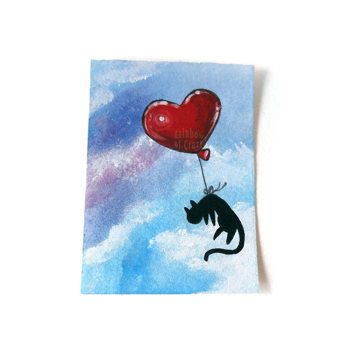 An ACEO painting of a black cat floating through a blue and purple sky, tied to a red heart balloon