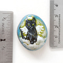 Load image into Gallery viewer, Rock art of a black cat as an angel, painted on a small beach stone, next to two rulers to show its size: 1 5/16&quot; x 1 1/8&quot; or 3.4 cm x 2.8 cm
