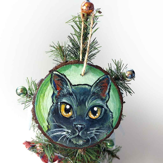 a round wood ornament, hand painted with a portrrait of a black cat's face, with yellow eyes, against a soft green background