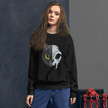 Load image into Gallery viewer, A woman is wearing a unisex sweatshirt in the colour black, printed with a graphic of a split image: the left side features a yellow eyed black cat, and the right side features an evil looking cat skull
