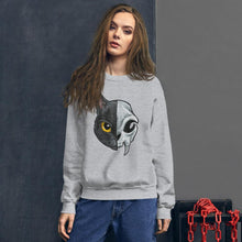 Load image into Gallery viewer, A woman is wearing a unisex sweatshirt in the colour sport grey, printed with art of a split image: the left side features a yellow eyed black cat, and the right side features an evil looking cat skull
