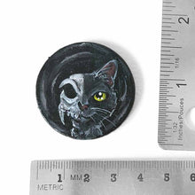 Load image into Gallery viewer, a circle shaped wood disc, hand painted with a split image: a black cat&#39;s face on the right side, and a cat skull on the left side. available as a keepsake or pendant necklace
