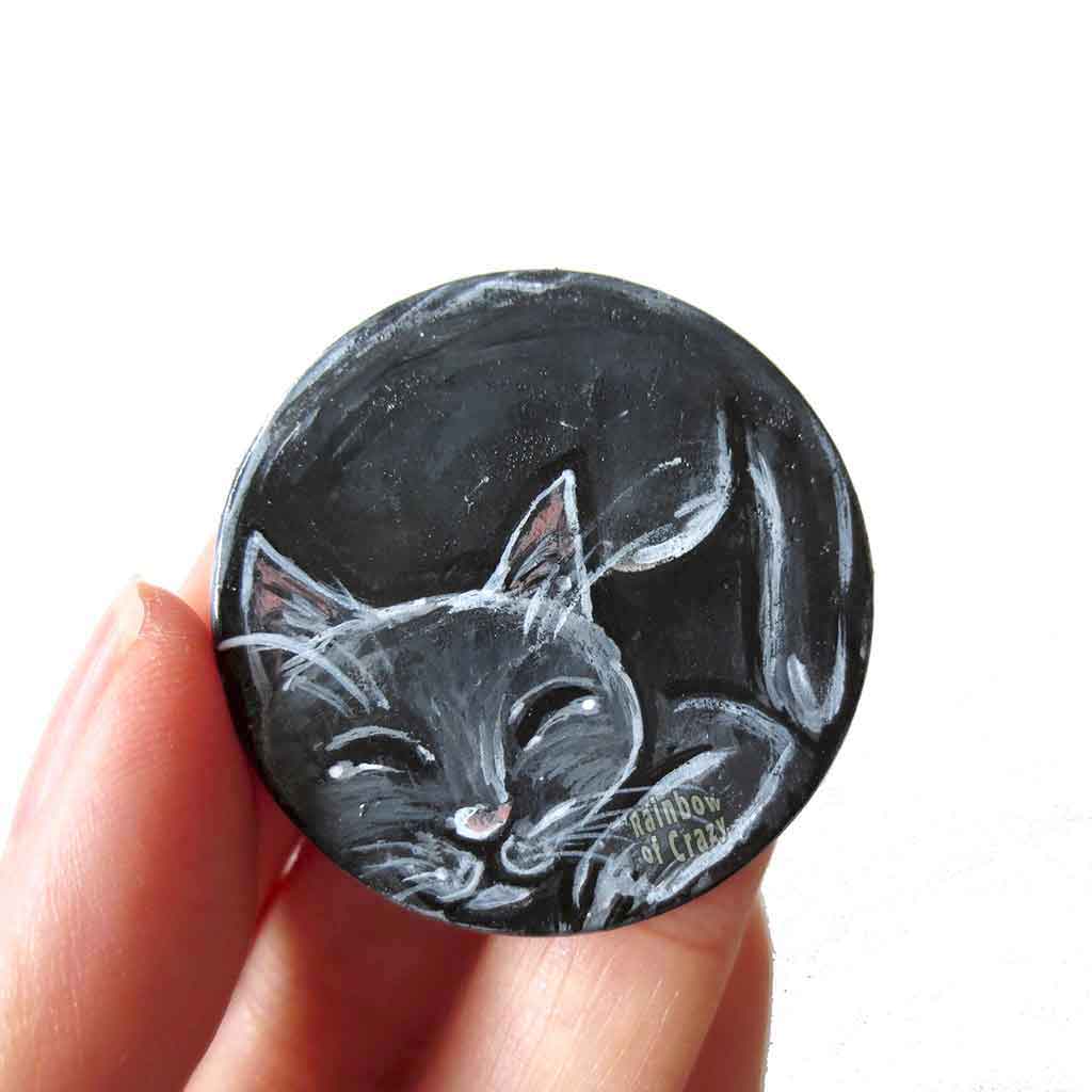 a wood circle, hand painted with a sleeping black cat, available as a keepsake or necklace pendant with chain.