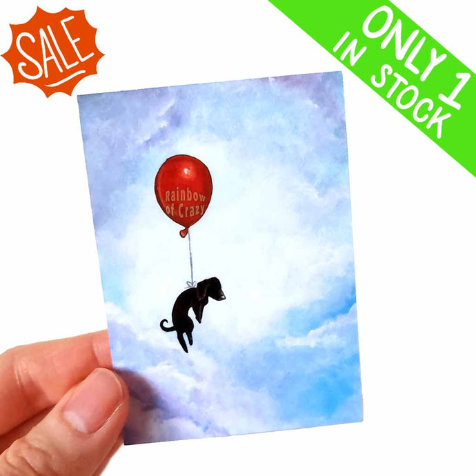 This aceo  art print features a black dachshund floating through the cloudy blue sky with a red balloon. 