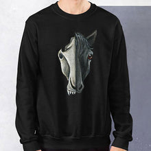Load image into Gallery viewer, A man is wearing a unisex sweatshirt in the colour black, which is printed with a split graphic: the right side features the face of a black horse, and the left side features an evil looking horse skull
