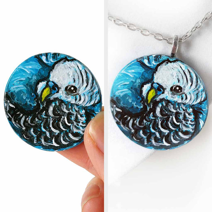 a small wood circle, hand painted with the portrait of a blue budgie bird, available as a keepsake or pendant necklace