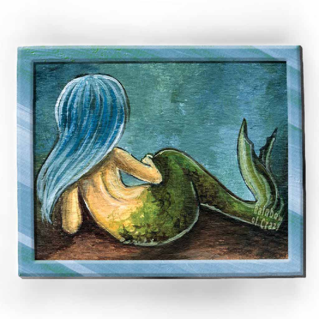 An art print of a mermaid with ice blue hair, lying down on the ocean floor, facing away.