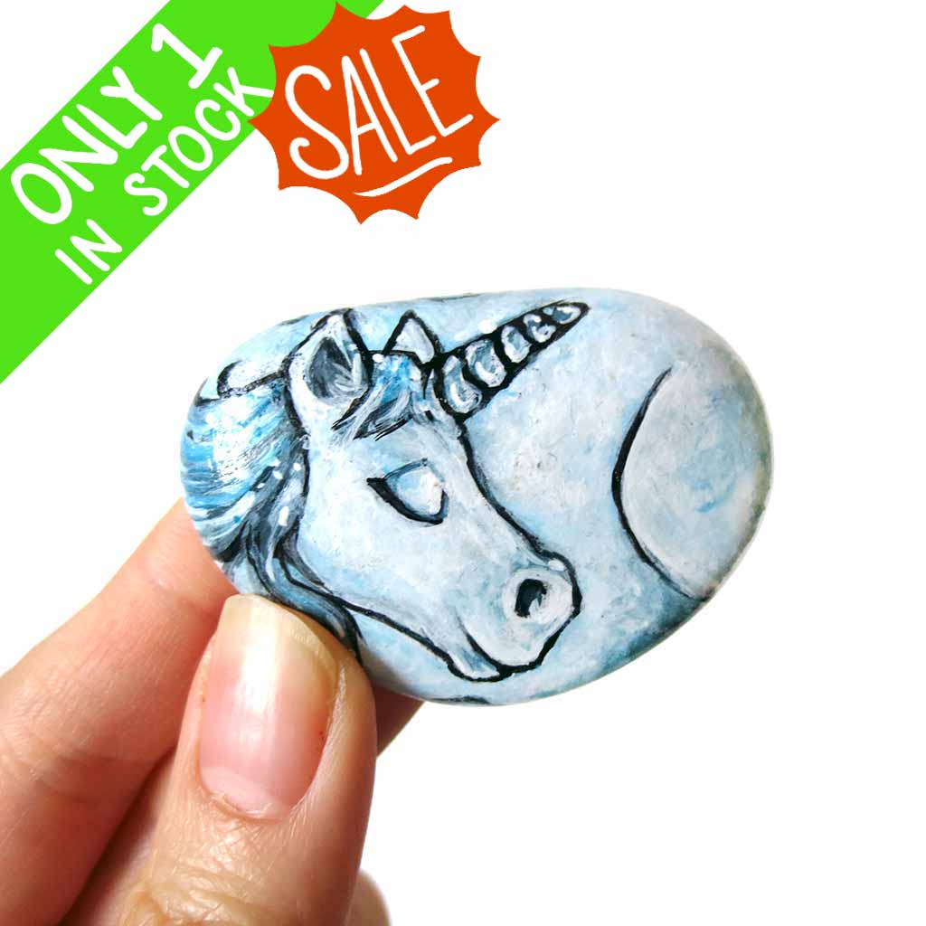 small rock art hand painted with the portrait of a light blue unicorn with its eyes closed 