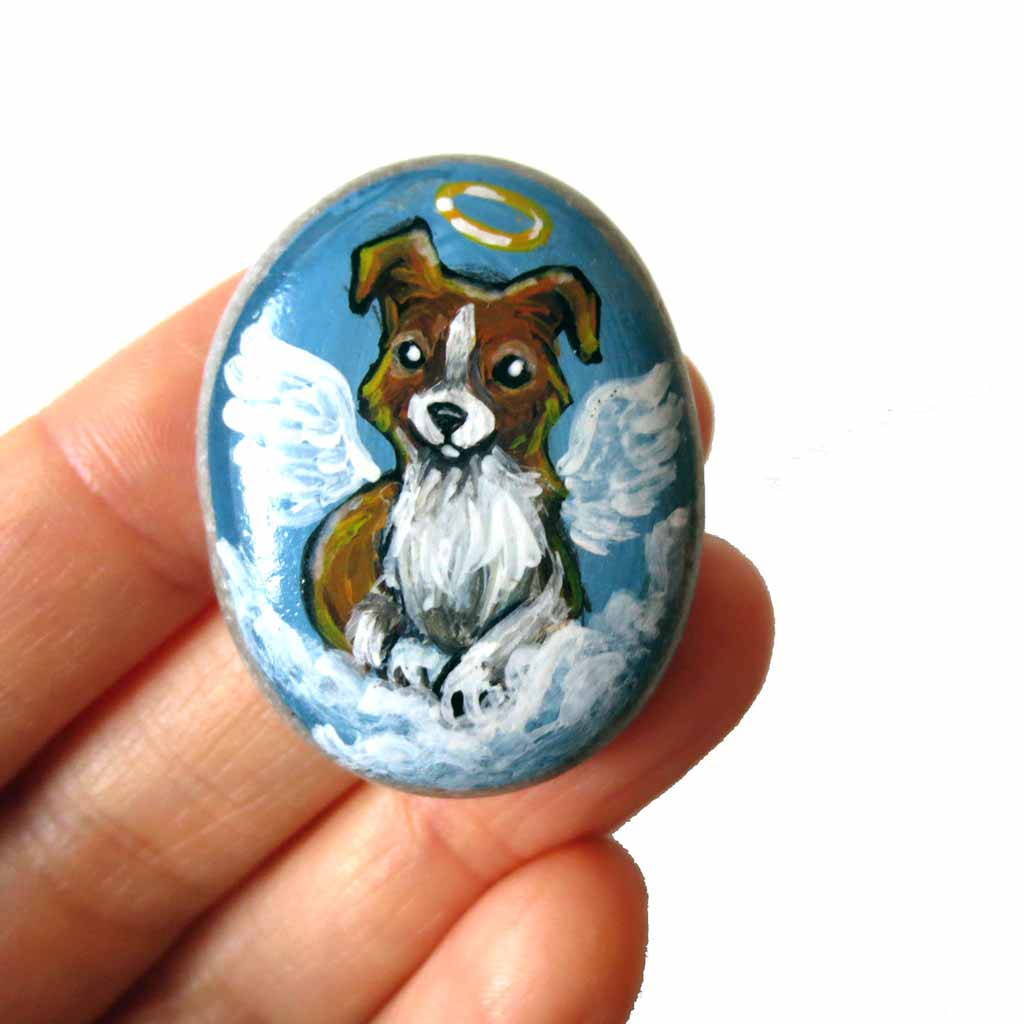Small rock art of a border collie, painted as an angel, with halo and wings, sitting on clouds. available as a keepsake or pendant necklace