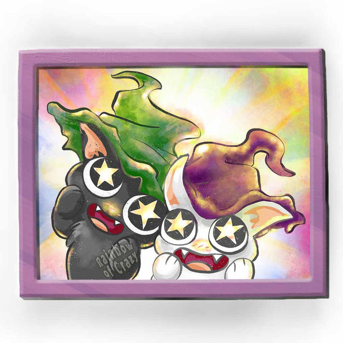 an art print featuring an illustration of a black cat wearing a green witch hat, and a white cat wearing a purple witch hat. with stars in their eyes, they're looking at the viewer in awe.