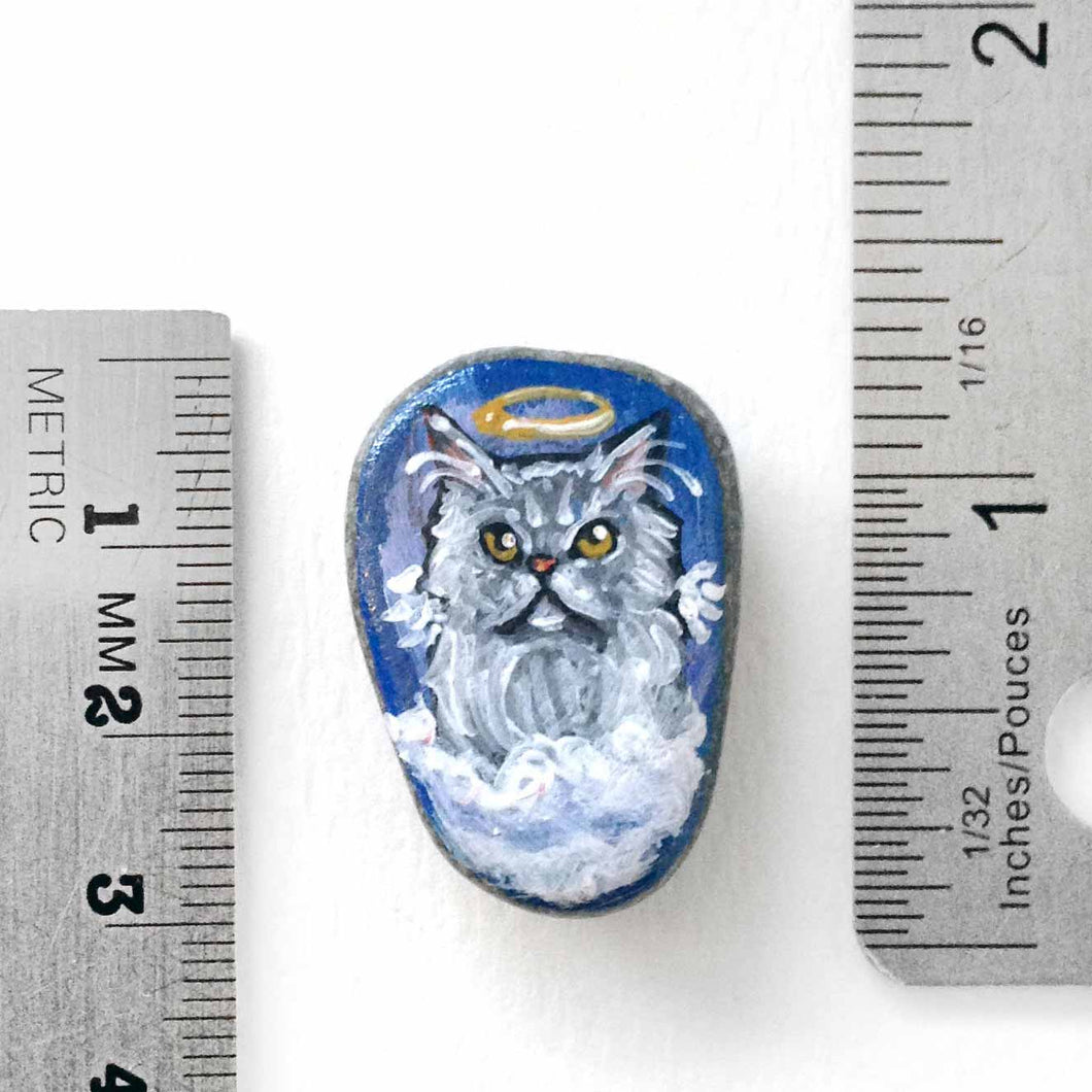 a small beach stone hand painted with the portrait of a grey Persian cat, as an angel on the clouds. available as a keepsake or pendant necklace