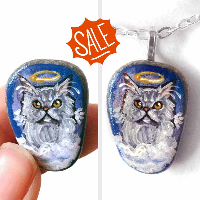 a small beach stone hand painted with the portrait of a grey Persian cat, as an angel on the clouds. available as a keepsake or pendant necklace