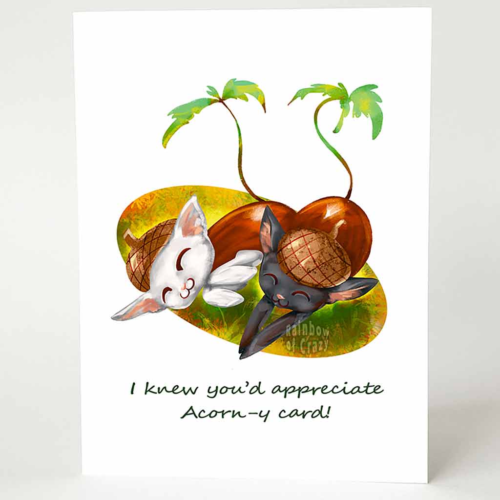 a pun-y greeting card with an illustration of a white cat and black cat, both sleeping, dressed up as acorns, complete with sprouting leafy tails. the card reads, 'I knew you'd appreciate Acorn-y card!