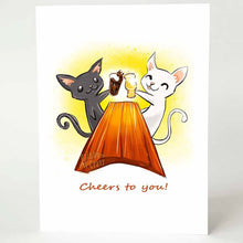 Load image into Gallery viewer, a greeting card, with art of a black cat and white cat toasting each other&#39;s beer glasses while sitting at a large wooden table. the card reads, &#39;cheers to you!&#39;
