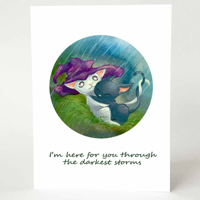 A sympathy card featuring an illustration of a white cat with a purple witch hat, holding tightly onto a scared black cat, as the hat protects them both from the pouring rain.