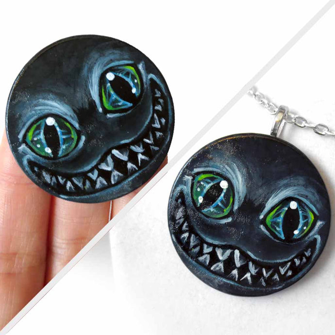 a portrait of an evil looking Cheshire Cat with an evil smile, hand painted on a wood disc. it's available as a keepsake or pendant necklace