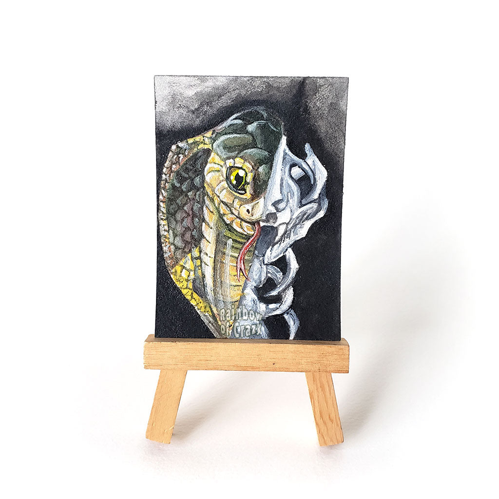 This ACEO sized painting features a split portrait: a Cobra snake on the left side, and a snake skull on the right. 