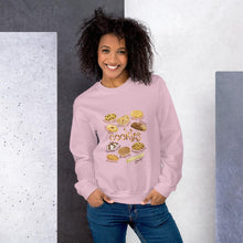 Load image into Gallery viewer, A woman wearing the Cookie Lovers Unisex Sweatshirt in the colour light pink, which features artwork of 10 types of cookies
