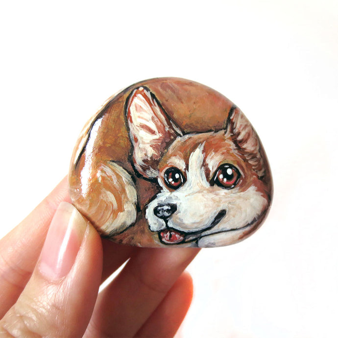 a beach rock with dog art: a portrait painting of a smiling corgi with its tongue sticking out