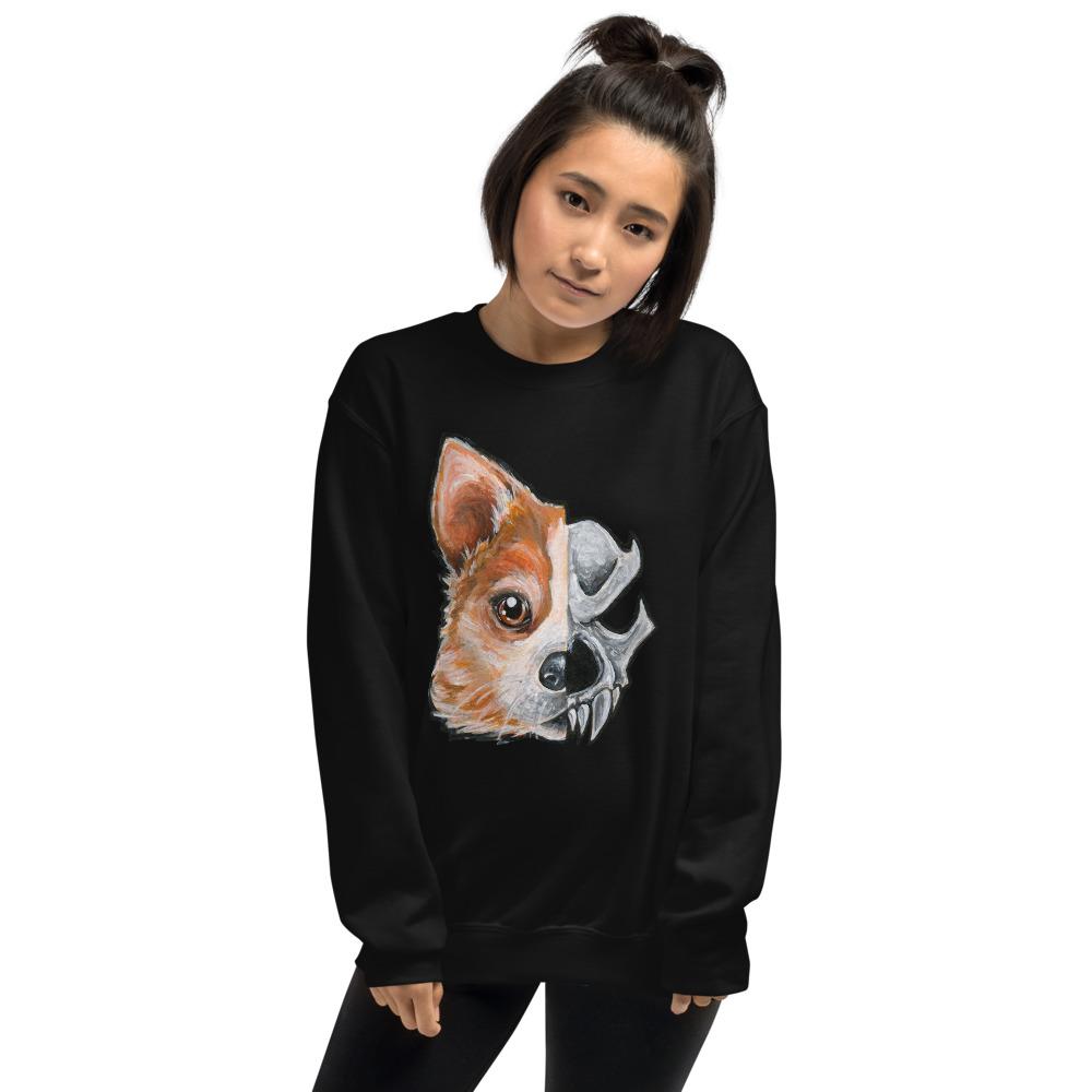 A woman is wearing a unisex sweatshirt in the colour black, which is printed with a split graphic: the left side features the face of a corgi dog, and the right side features an evil looking skull