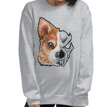 Load image into Gallery viewer, A woman is wearing a unisex sweatshirt in the colour sport grey, which is printed with a split graphic: the left side features the face of a corgi dog, and the right side features an evil looking skull
