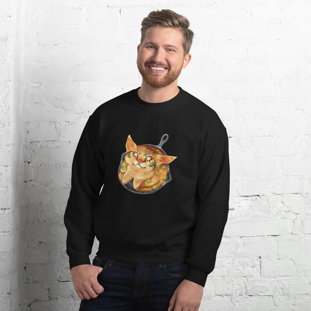 A man is wearing a unisex sweatshirt in the colour black, featuring artwork of a cornbread cat with jalapenos, sitting in a cast iron pan.
