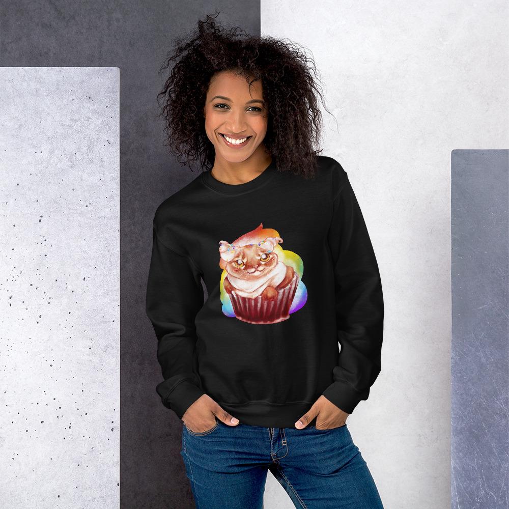 A woman wears a unisex sweatshirt in the colour black, featuring an illustration of a cat painted as a red velvet cupcake with rainbow sprinkles.