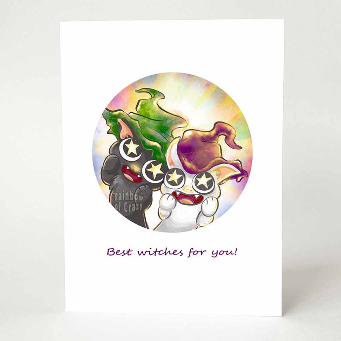 A greeting card with art of a black cat with a green witch hat, and a white cat with a purple witch hat, staring adoringly at the viewer with stars in their eyes. The card reads, Best witches for you!