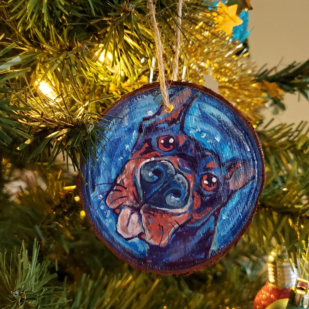 A Christmas wood ornament, featuring a painting of a doberman with a big blop of the tongue.